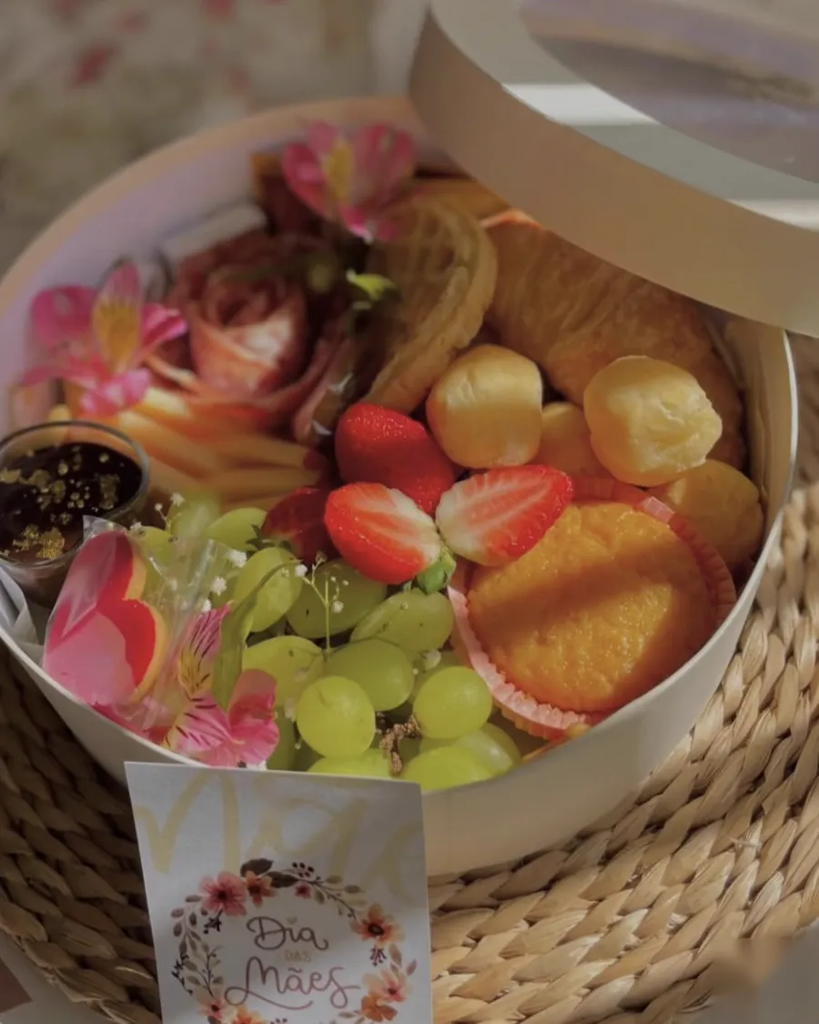 Caixa redonda de café da manhã com croissant, morangos, uvas e flores naturais