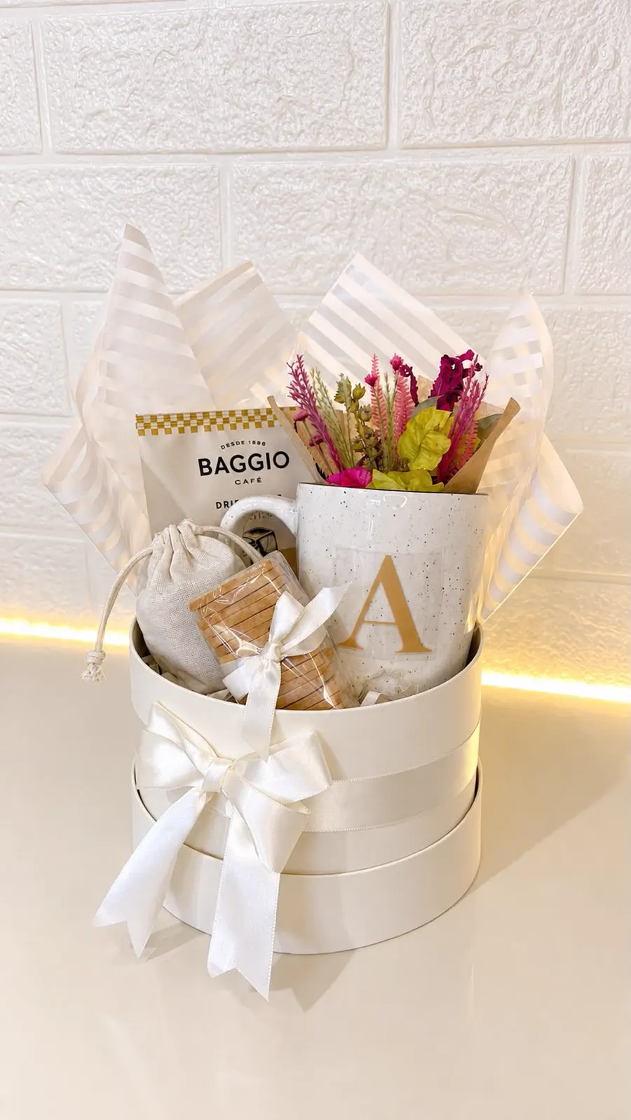 Cesta de presente montada: caixa redonda creme com laço, caneca com a inicial, café e flores secas