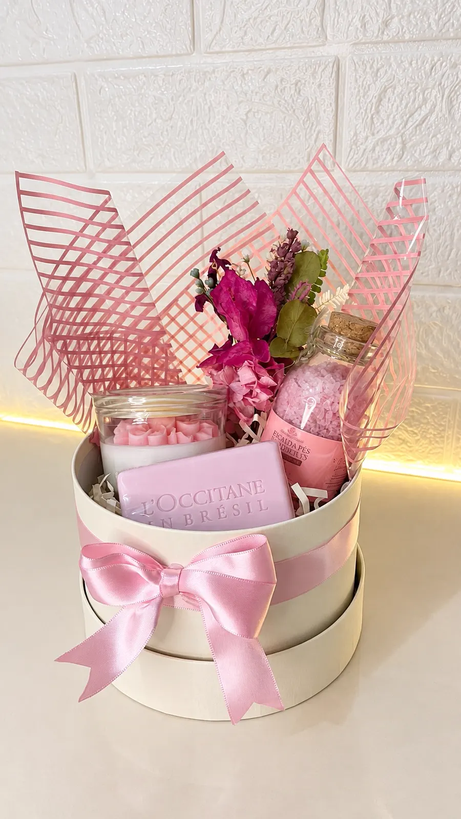 Cesta montada com laço rosa, sabonete, vela e flores
